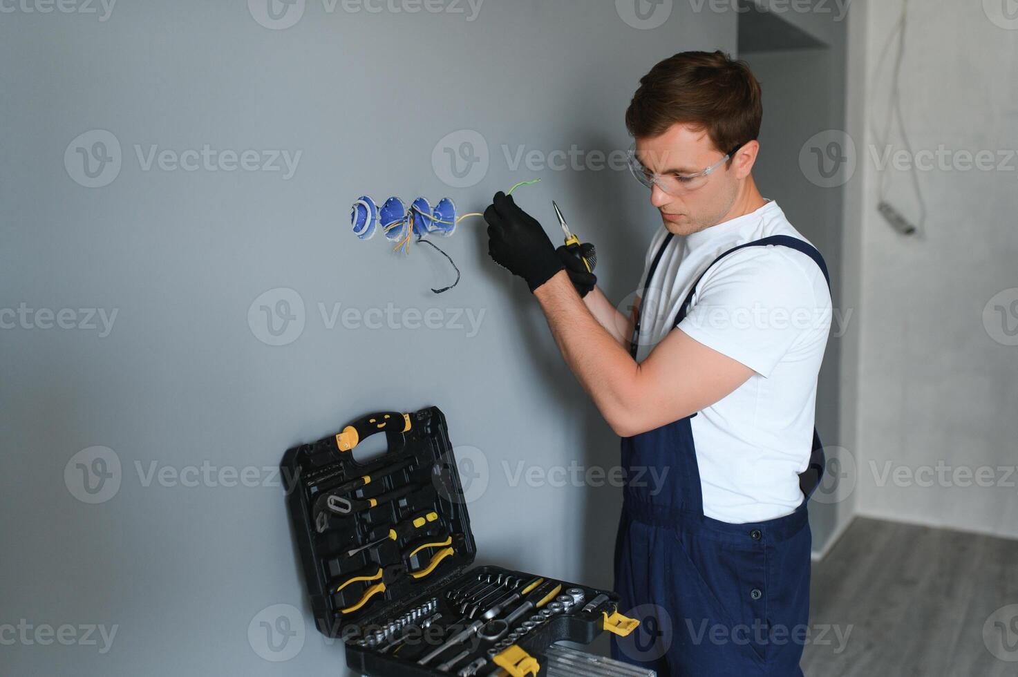 Electrician in uniform mounting electric sockets on the white wall indoors photo