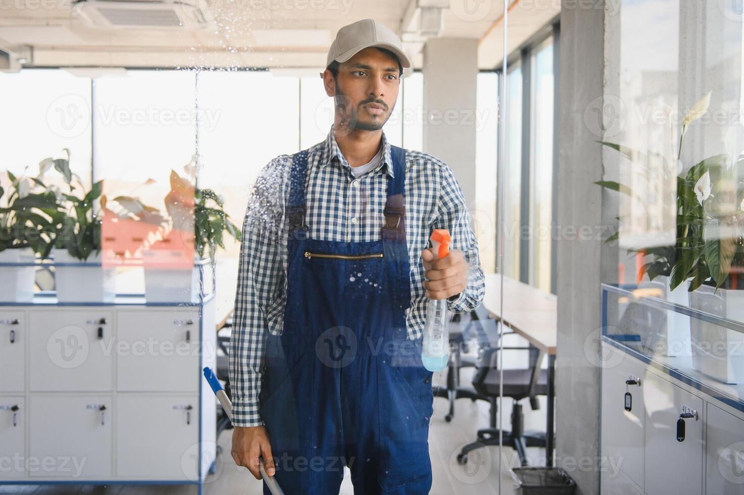 Young indian man washing window in office. photo