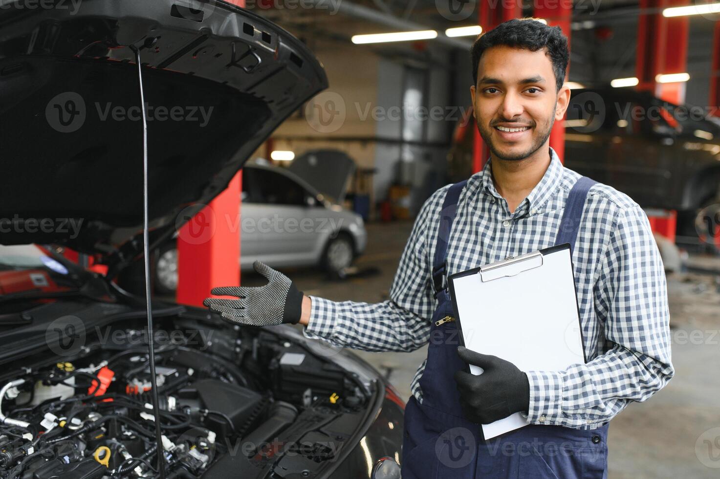 latin hispanic auto mechanic in uniform is examining a car while working in auto service photo
