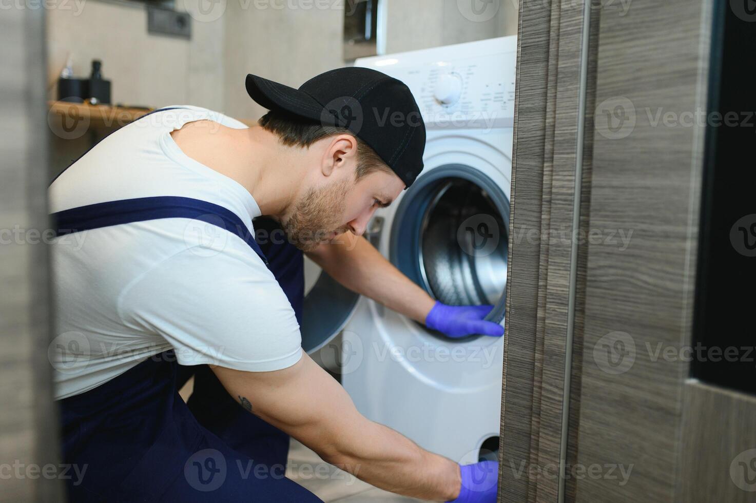 The young handsome repairman in worker suit with the professional tools box is fixing the washing machine in the bathroom photo