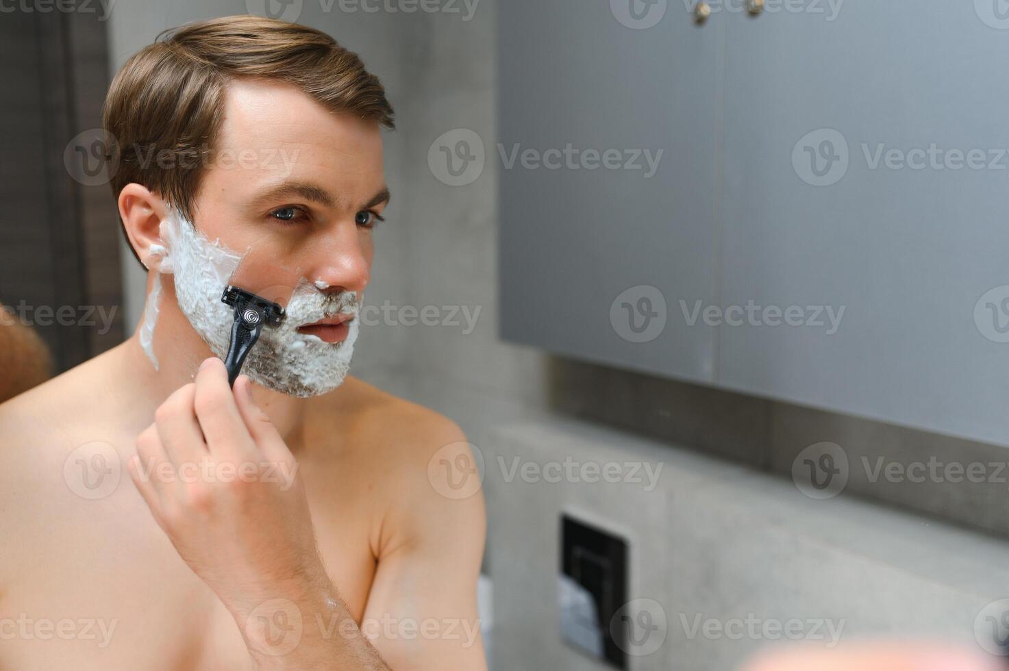 Mature handsome man shaving in front of mirror photo