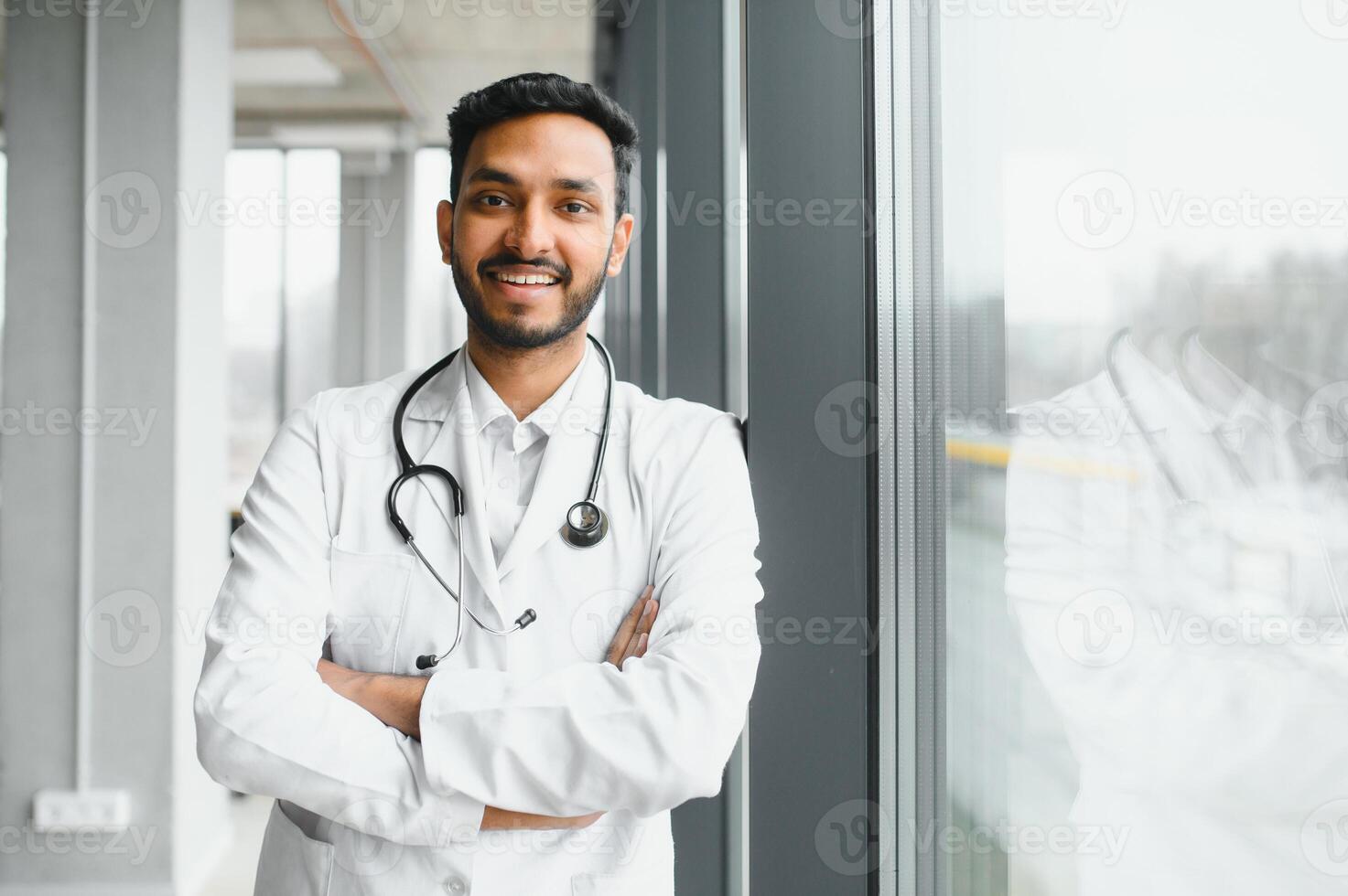 Portrait of male indian doctor wearing white coat having open door on clinic corridor as background photo