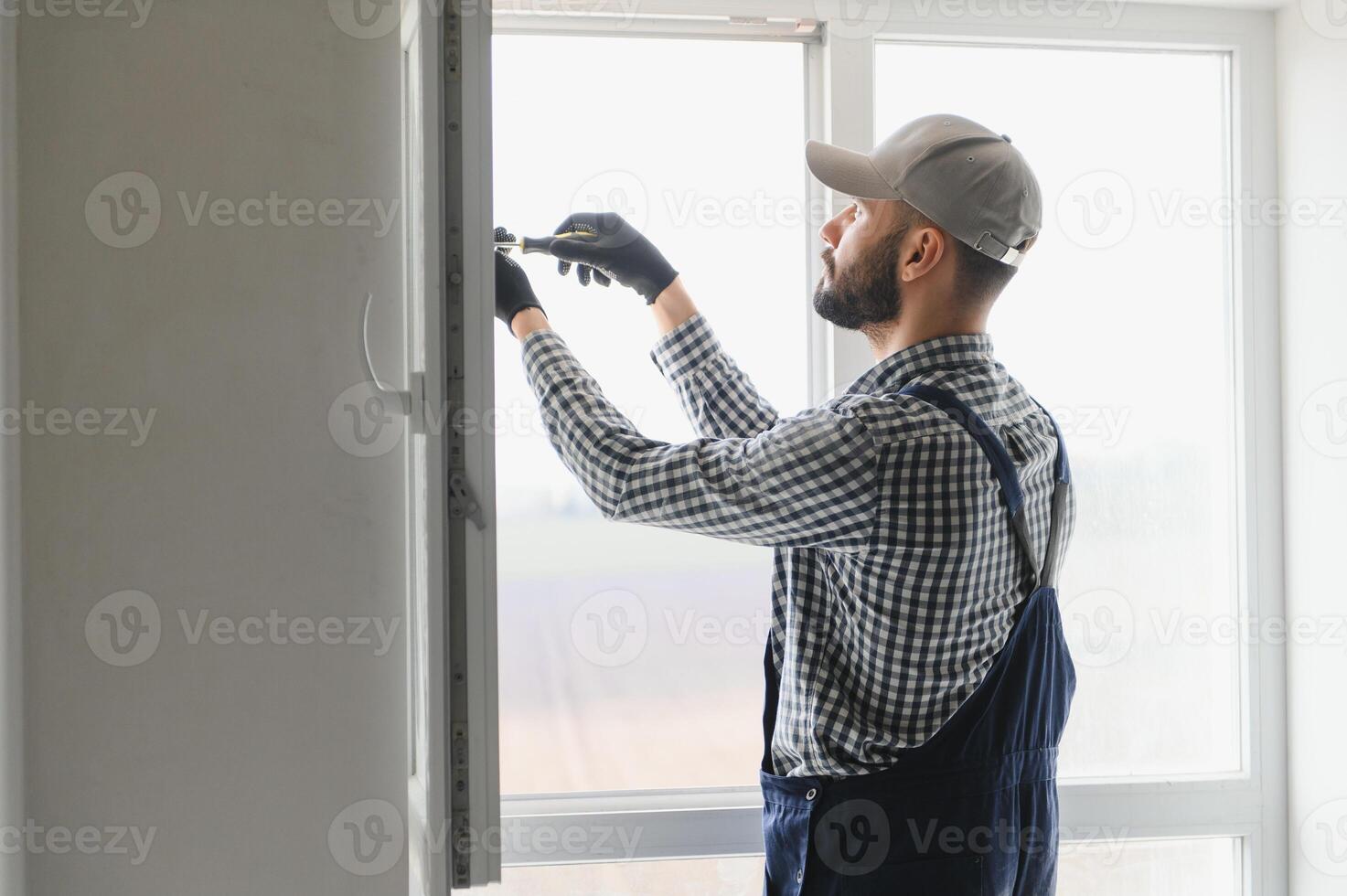 Workman in overalls installing or adjusting plastic windows in the living room at home photo
