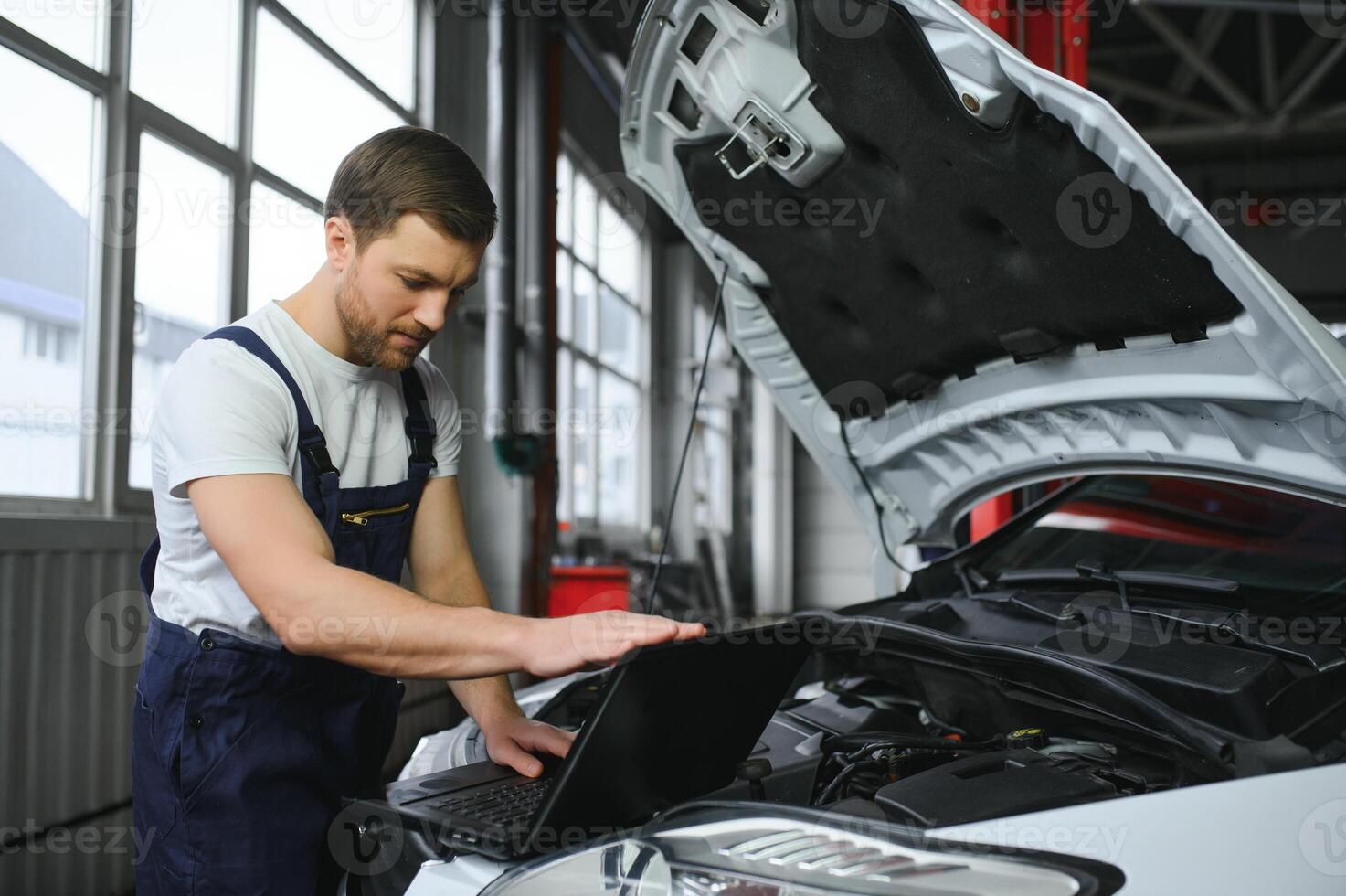 Mechanic man mechanic manager worker using a laptop computer checking car in workshop at auto car repair service center. Engineer young man looking at inspection vehicle details under car hood photo