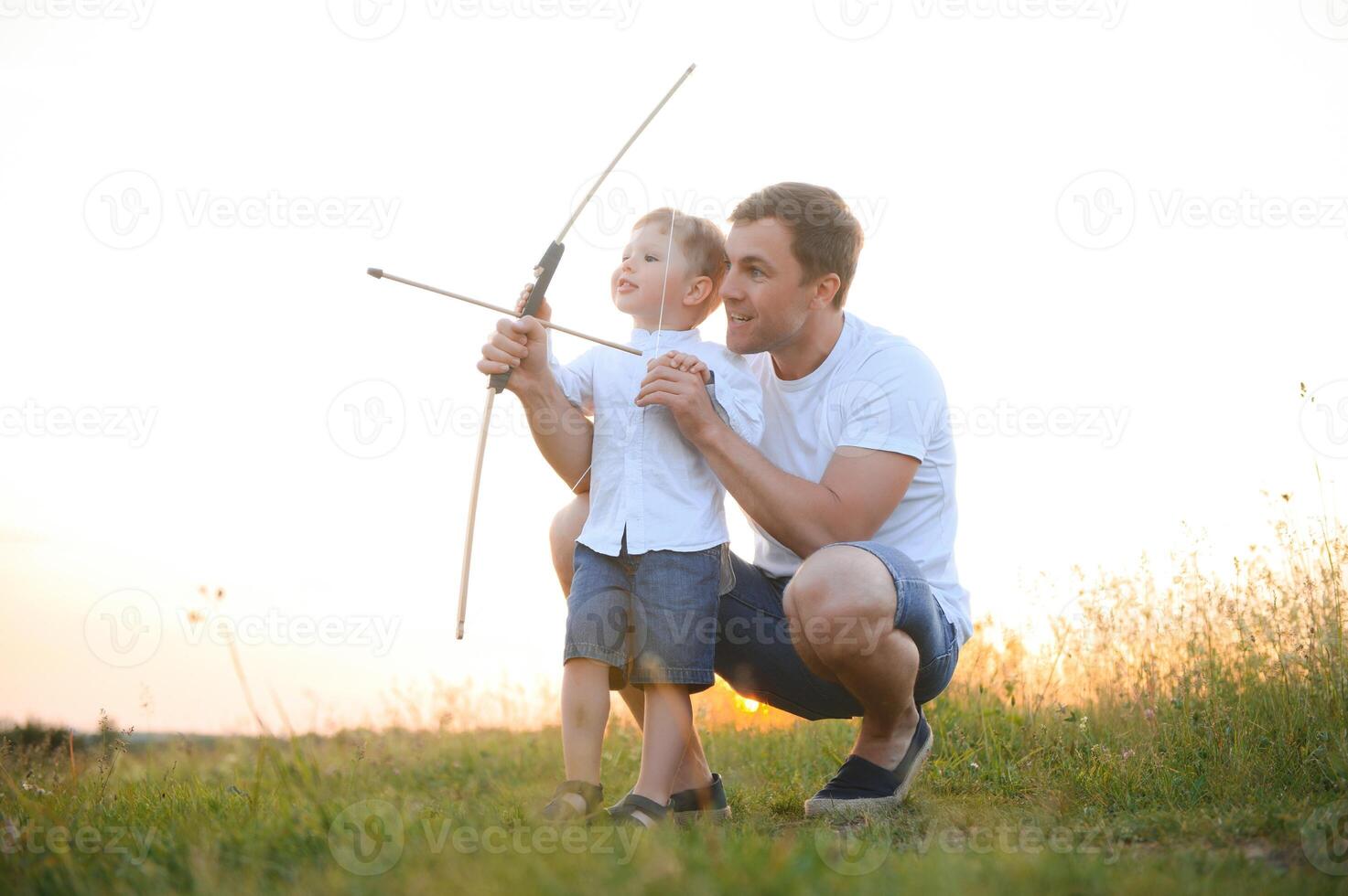 padre es aprendizaje su hijo a disparar desde arco en soleado verano día. foto