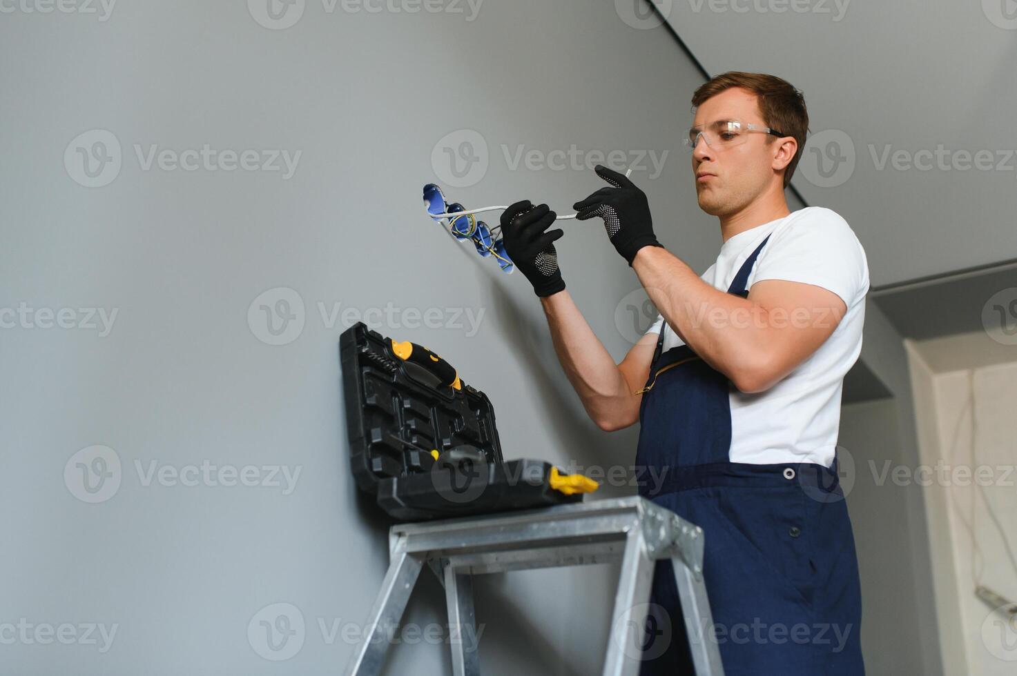 Electrician with screwdriver repairing power socket in room photo