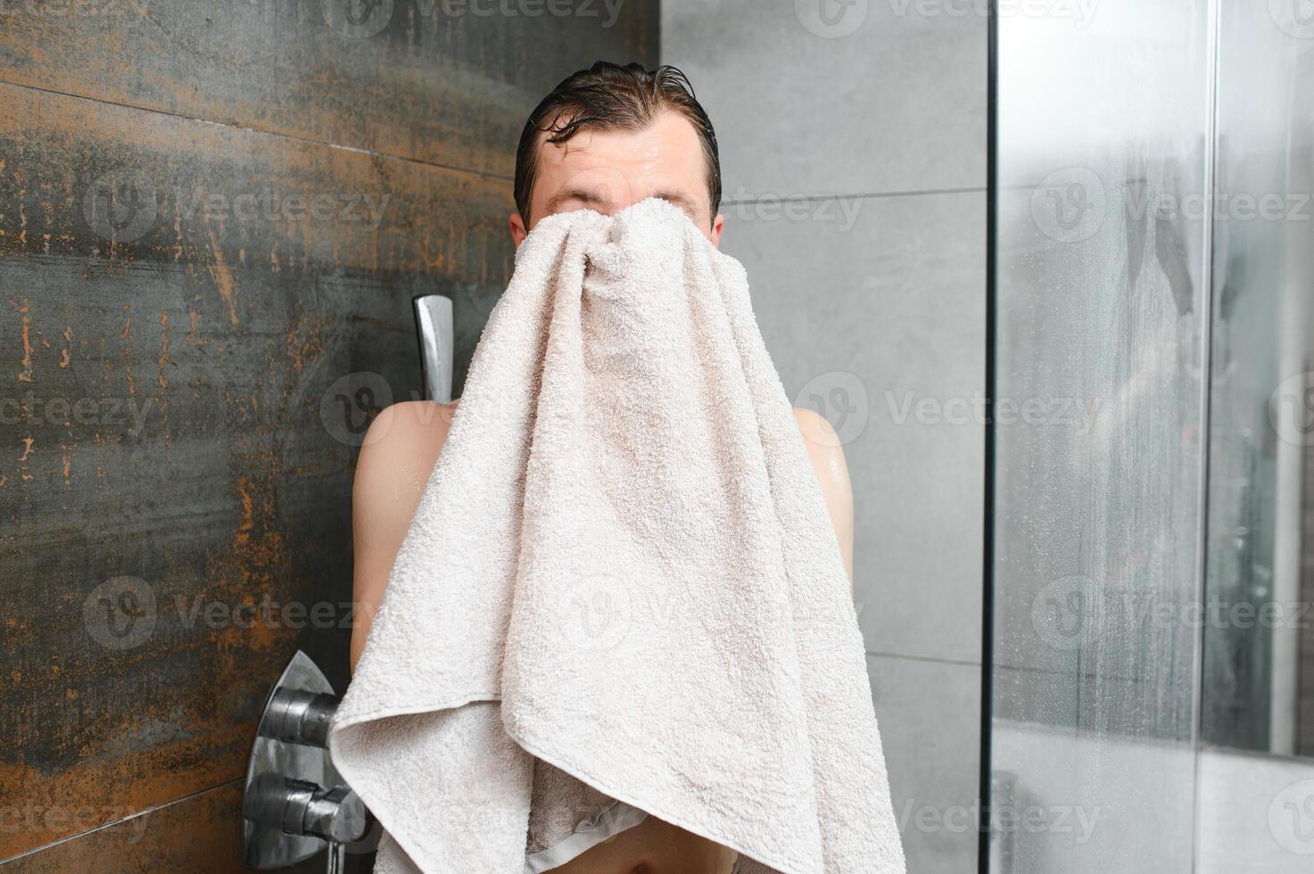 Cheerful young man wiping face with soft towel after washing it in the morning photo