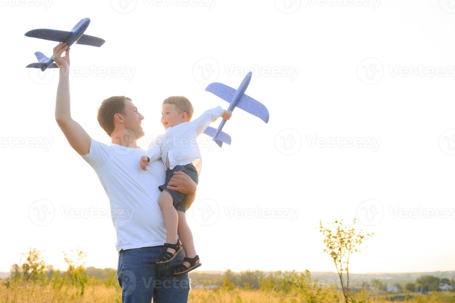Cute little boy and his handsome young dad are smiling while playing with a toy airplane in the park. photo