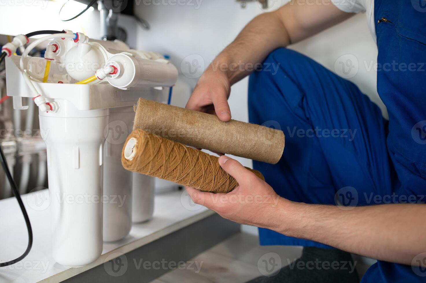 Plumber installs or change water filter. Replacement aqua filter. Repairman installing water filter cartridges in a kitchen. Installation of reverse osmosis water purification system. photo