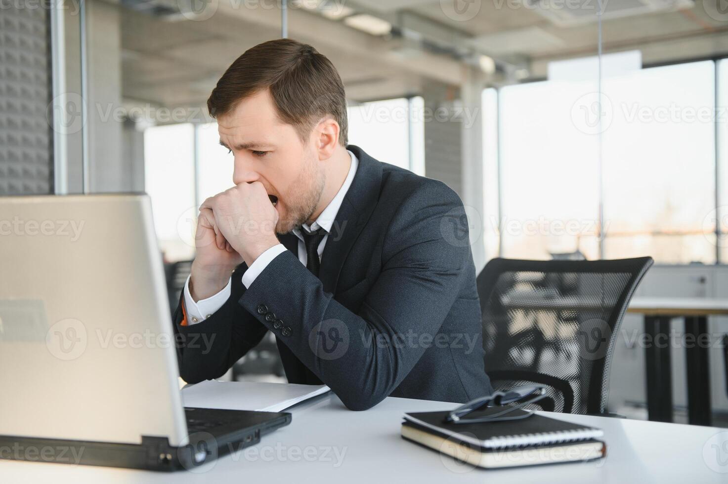 Depressed young businessman holding head in hands, has problem, a laptop on the desk. A guy made a mistake in a work photo