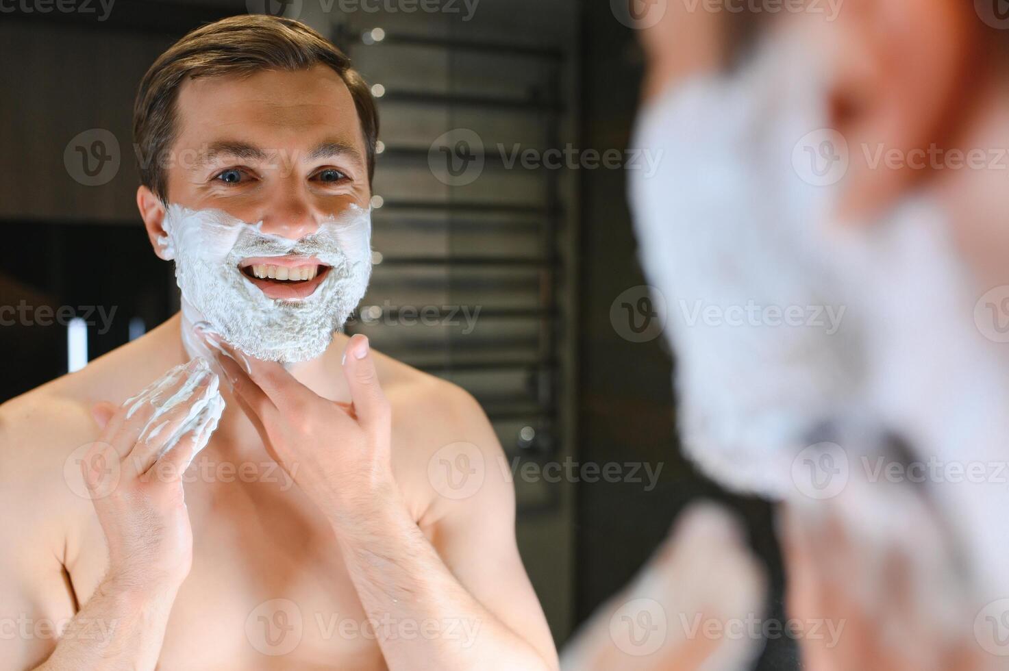 Shaving cream. Morning hygiene procedures. Grooming treatment. Handsome cheerful shirtless man showing applying foam on skin photo