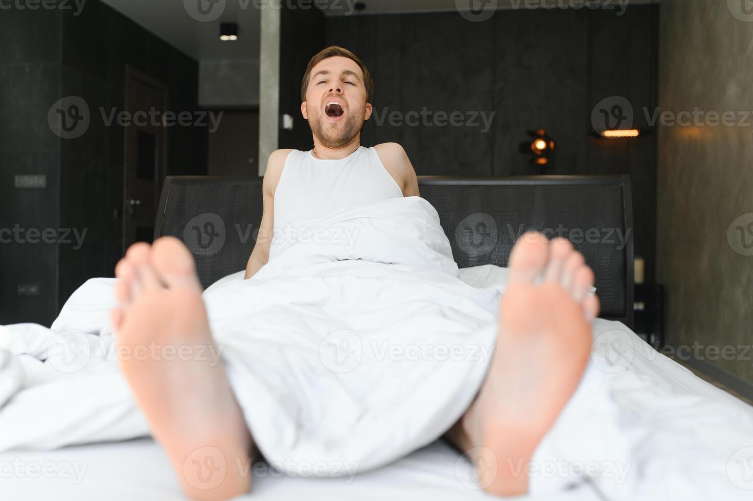 Cheerful Man Waking Up Lying In Cozy Bed At Home On Weekend Morning. Healthy Sleep Concept photo