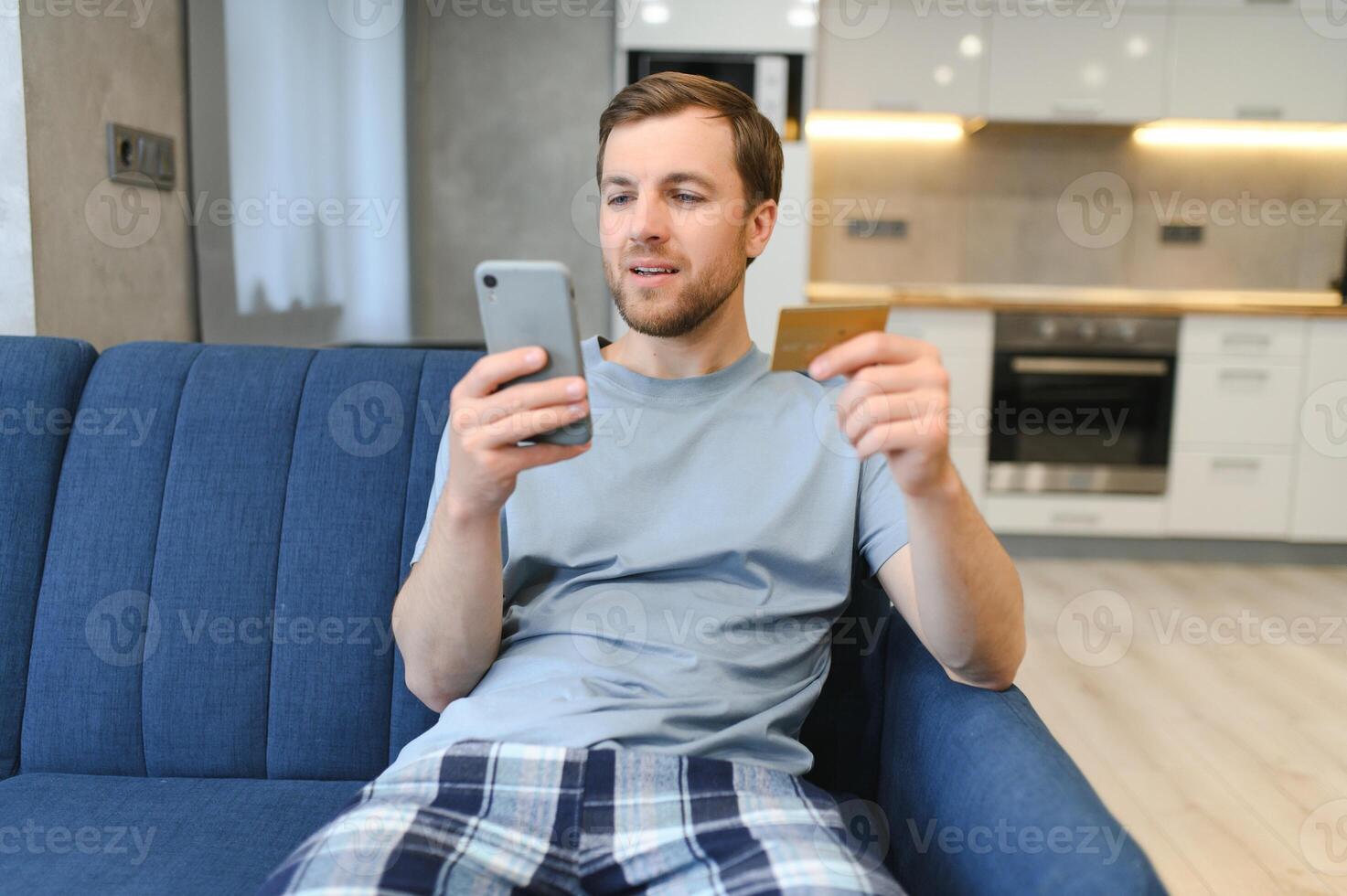 joven hombre sentado a hogar pago para comida en línea con teléfono inteligente y crédito tarjeta foto