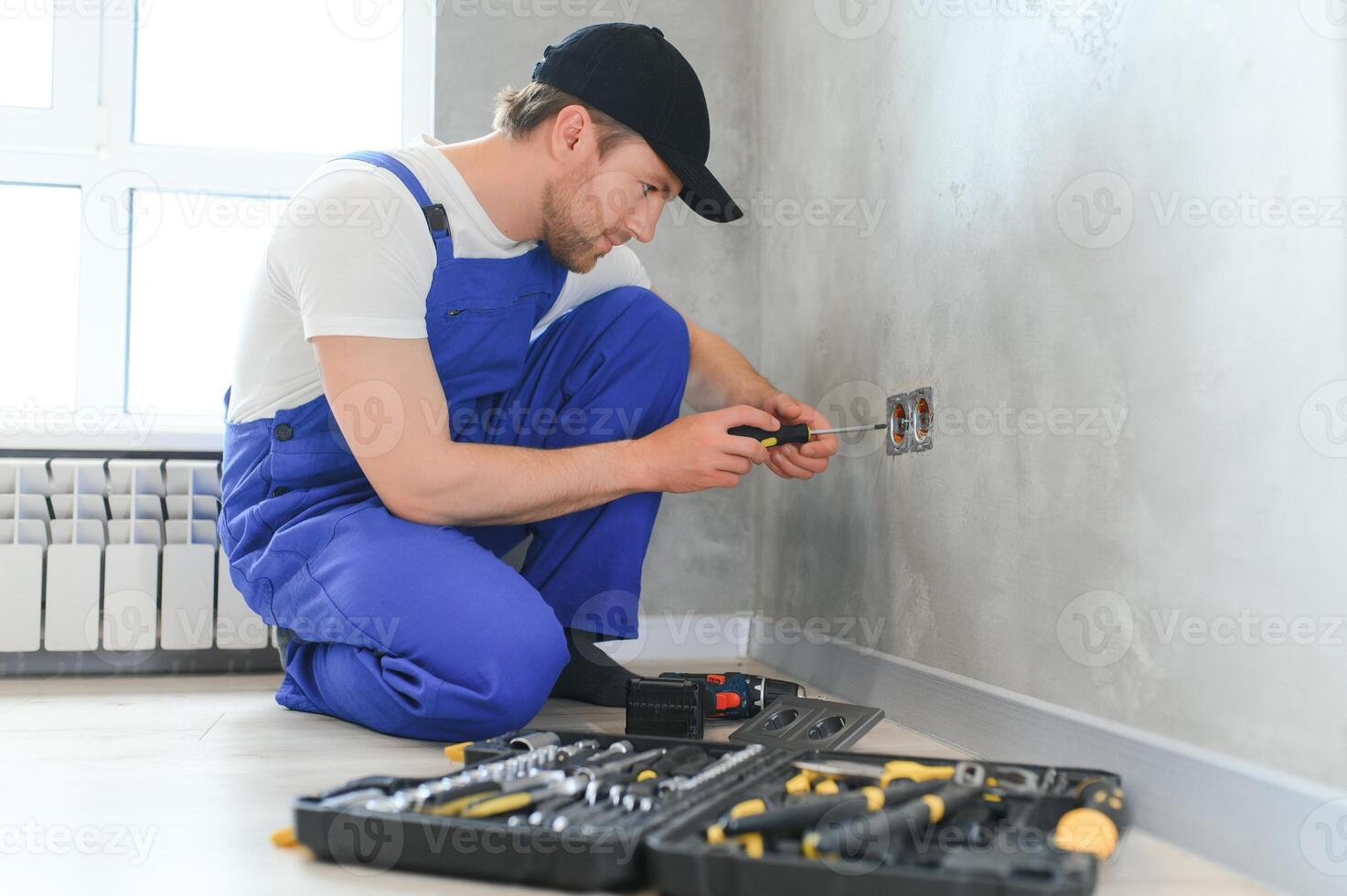 Professional electrician working on a home electrical system, he is installing a wall socket photo