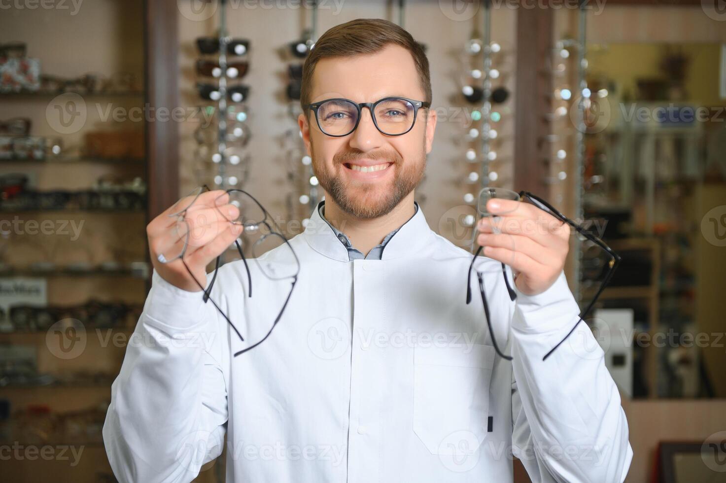Handsome ophthalmologist holding eyeglasses for a try out. Optometrist offering to wear a pair of glasses. photo