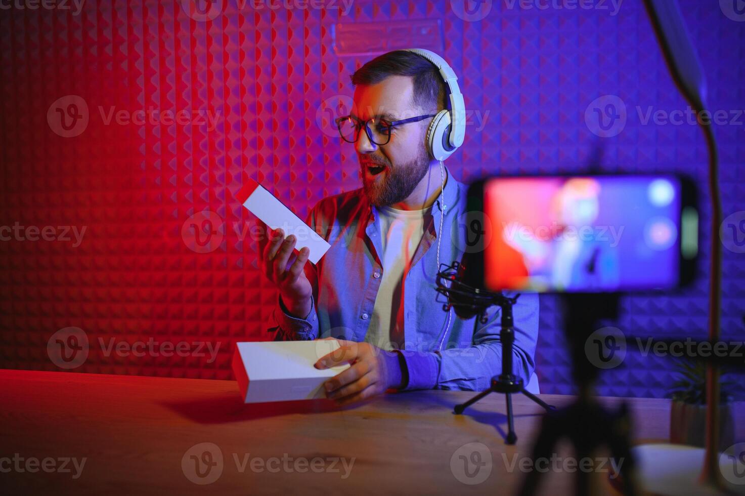 Male technology blogger recording video blog or vlog review of new smartphone, showing it on camera at home studio. Blogging, Work from Home concept. Selective focus. Web Banner photo