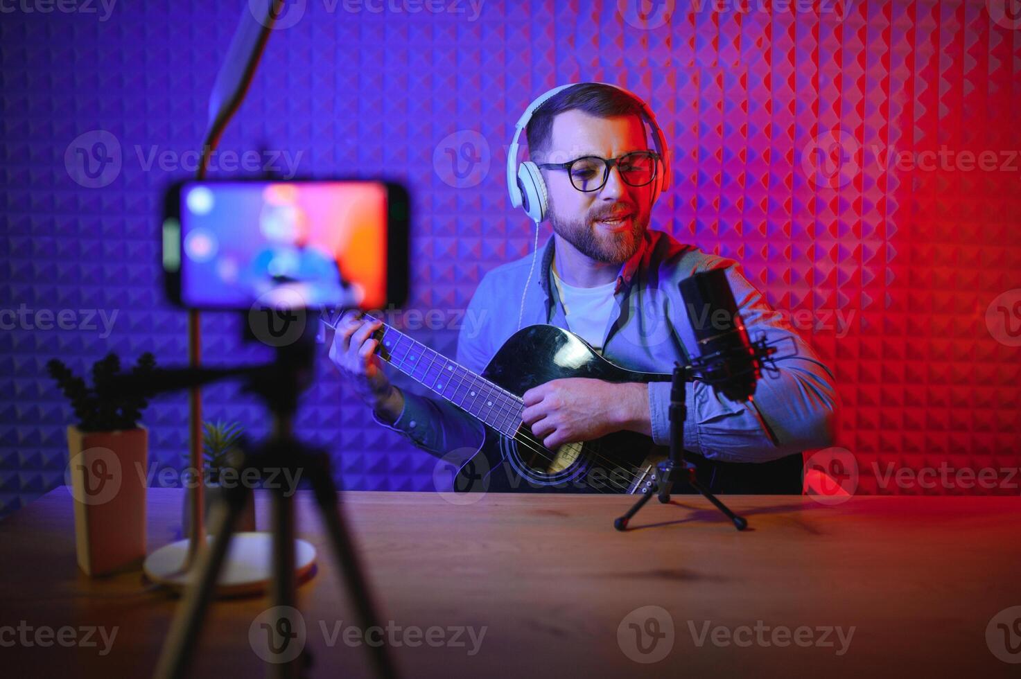 vlogger using smartphone to film podcast in studio. blogger with mobile phone, microphone and headphones filming video for social media broadcasting career. photo