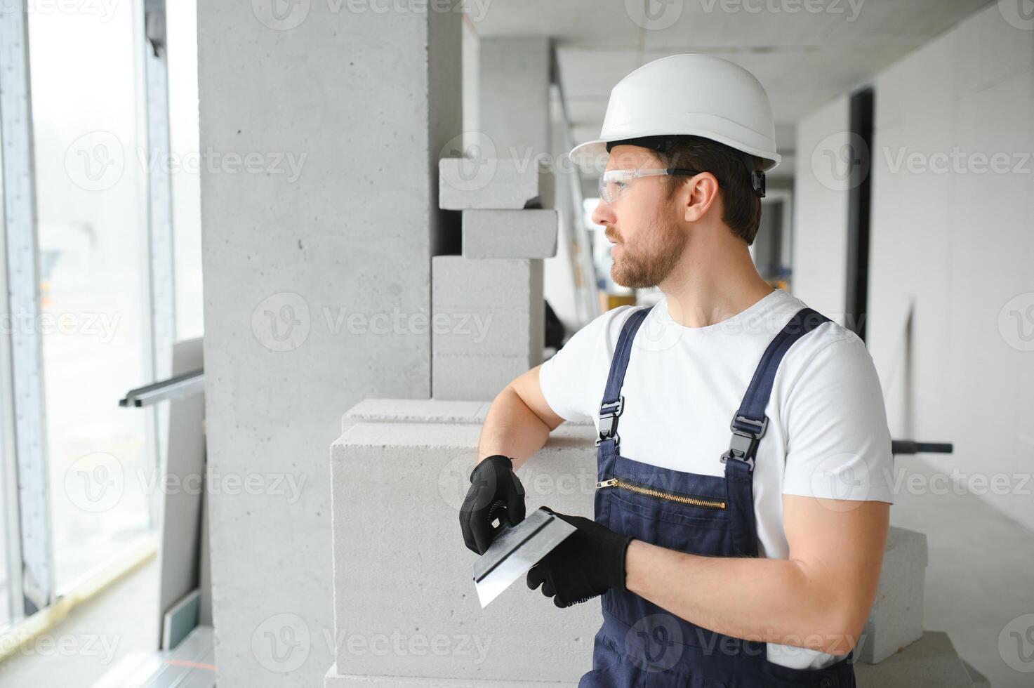 Portrait of a young foreman in uniform standing on a construction site indoors near a stepladder. photo