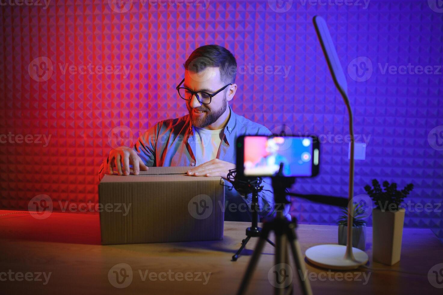 Handsome young man gesturing while unpacking parcel, excited, clenches fists in triumph. Joyful male vlogger. Concept of people and social networks. photo
