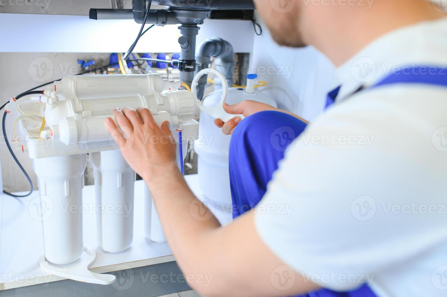 Plumber installs or change water filter. Replacement aqua filter. Repairman installing water filter cartridges in a kitchen. Installation of reverse osmosis water purification system. photo