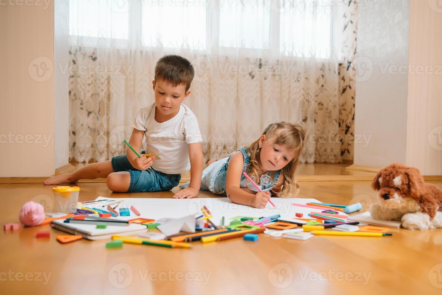 Kids drawing on floor on paper. Preschool boy and girl play on floor with educational toys - blocks, train, railroad, plane. Toys for preschool and kindergarten. Children at home or daycare photo