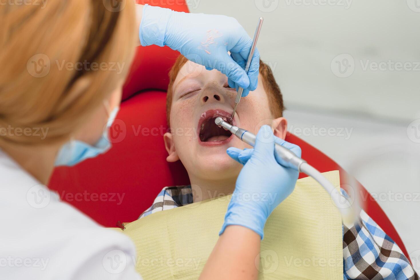 Pediatric dentist examining a little boys teeth in the dentists chair at the dental clinic photo