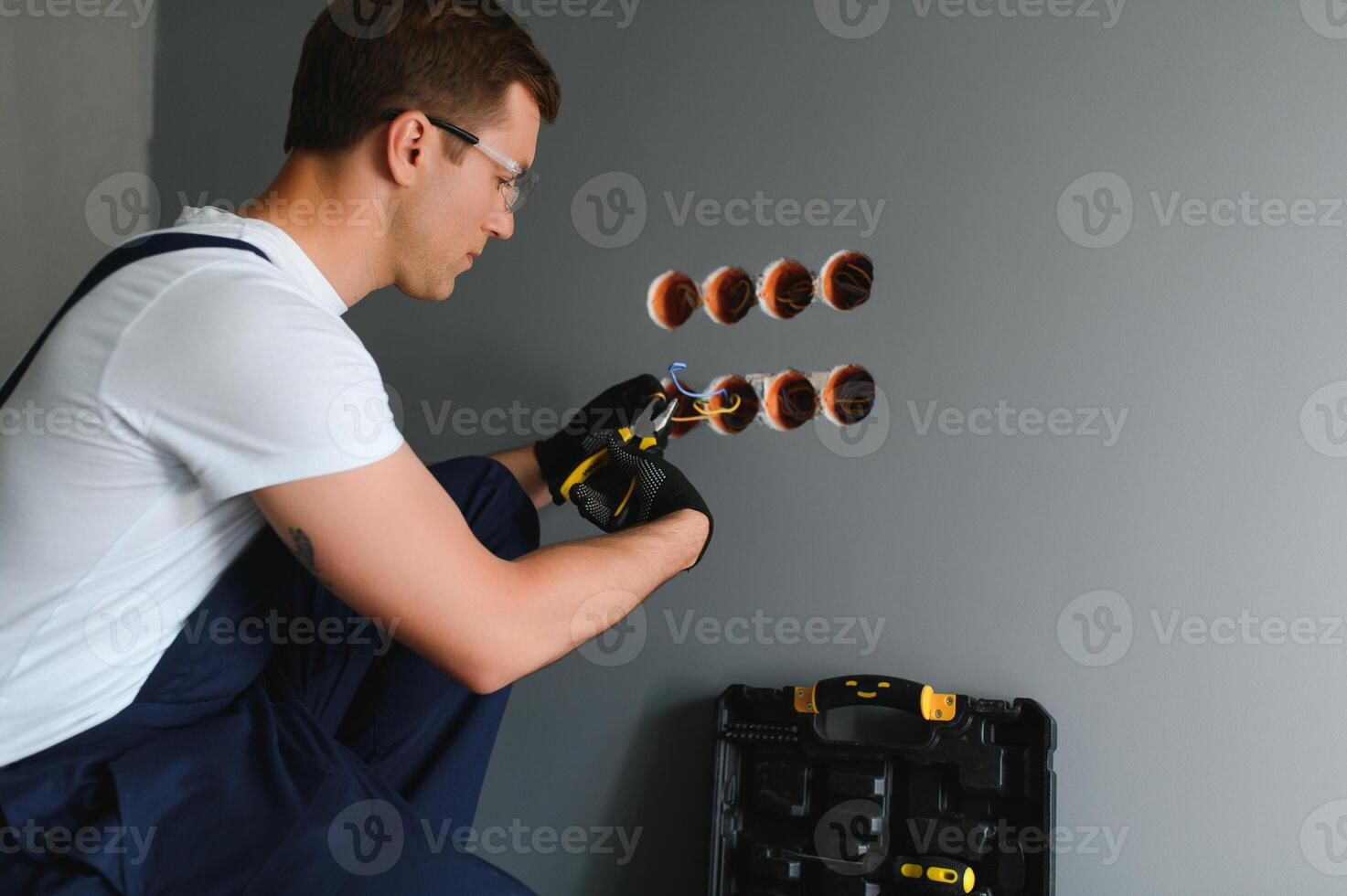 Electrician Builder at work, installation of sockets and switches. Professional in overalls with an electrician's tool. Against the background of the repair site. photo