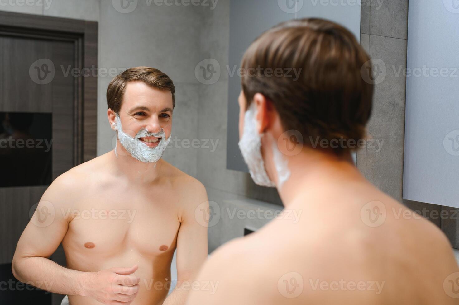 Mature handsome man shaving in front of mirror photo