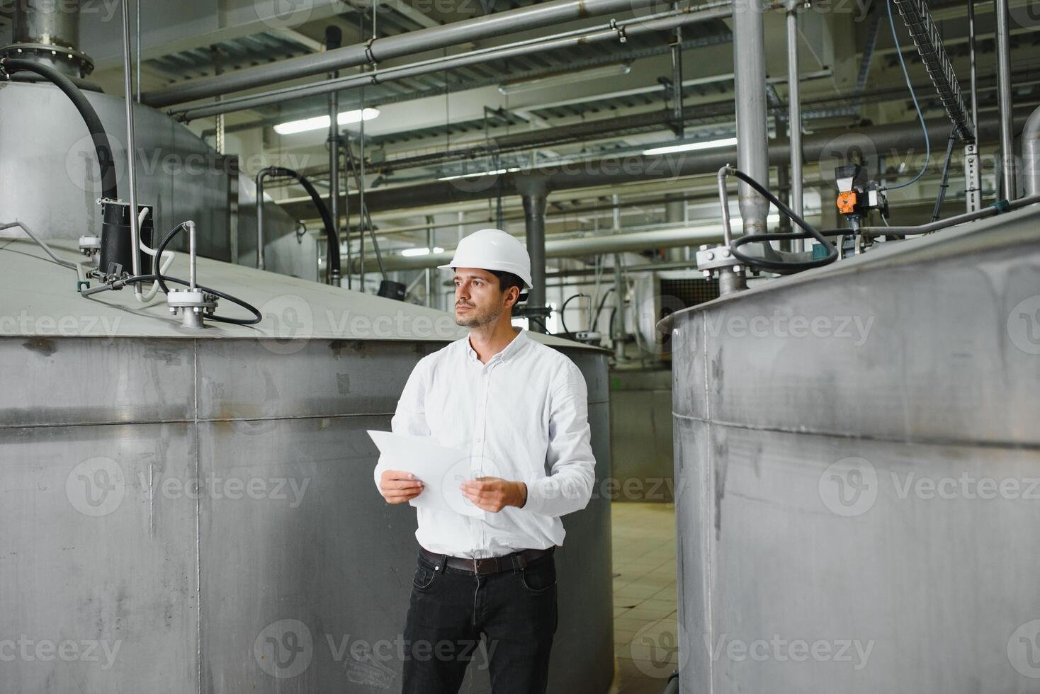 Smiling and happy employee. Industrial worker indoors in factory. Young technician with white hard hat. photo