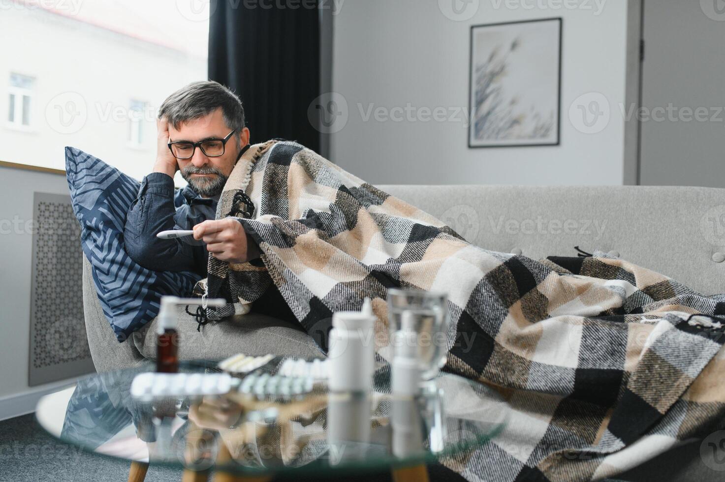 Sick senior man using thermometer checking his temperature suffering from seasonal flu or cold. photo