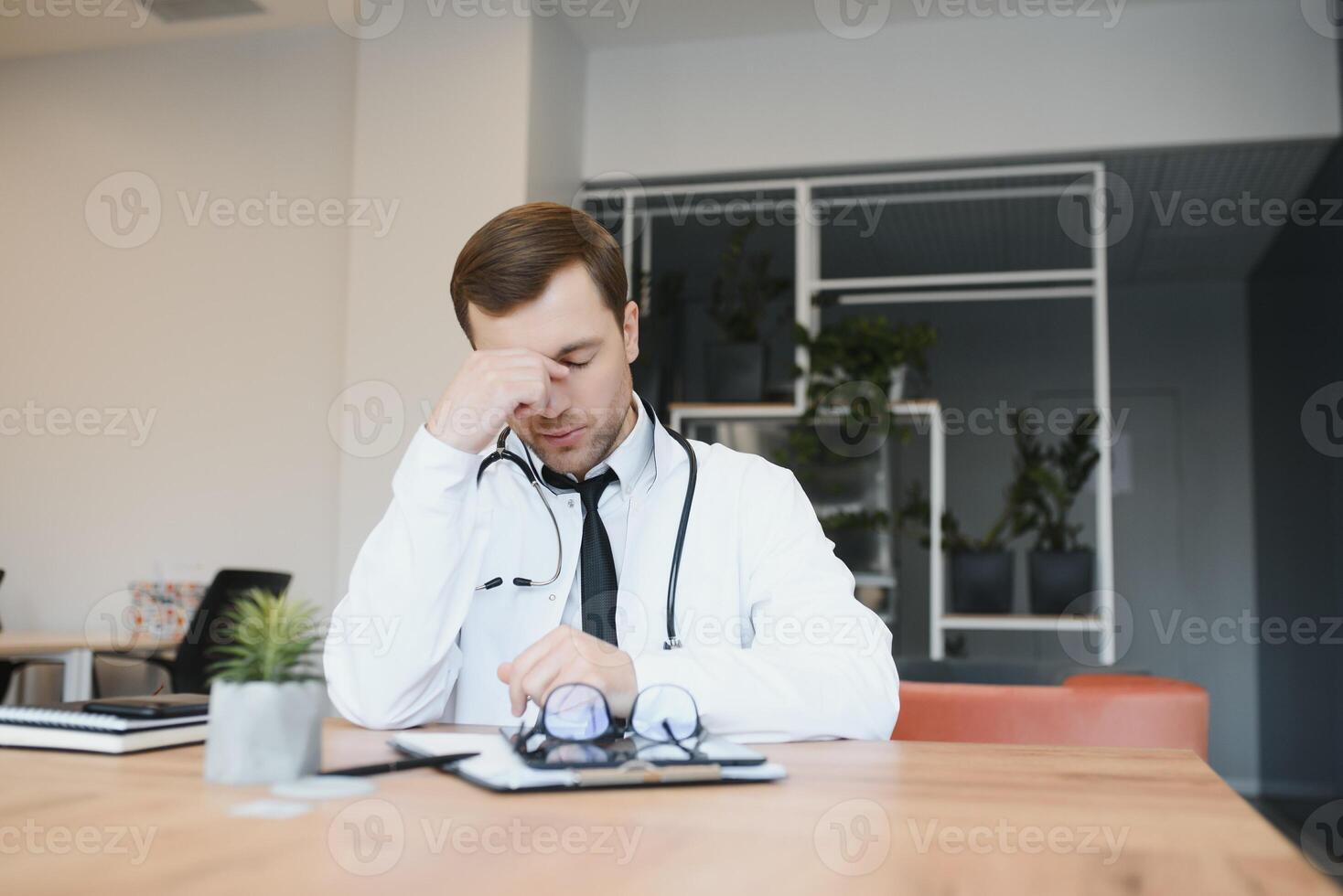 Stressed male doctor. Mid adult male doctor working long hours. Overworked doctor in his office. Not even doctors are exempt from burnout . photo