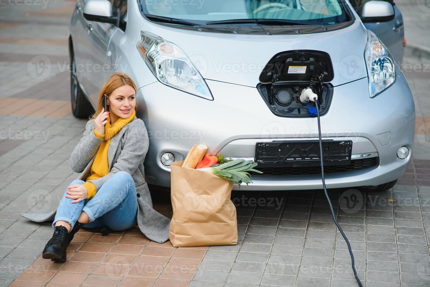 Using smartphone while waiting. Woman on the electric cars charge station at daytime. Brand new vehicle photo