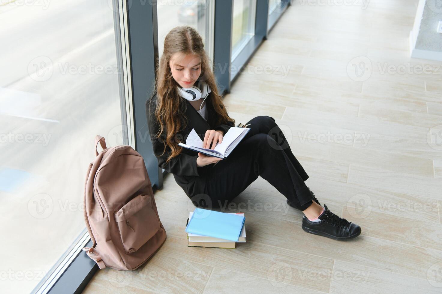 niña sonriente. hermosa Chica de escuela sonriente mientras sentado cerca ventana y leyendo libro foto