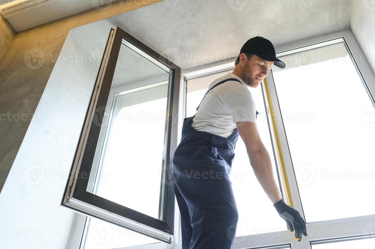 Workman in overalls installing or adjusting plastic windows in the living room at home photo