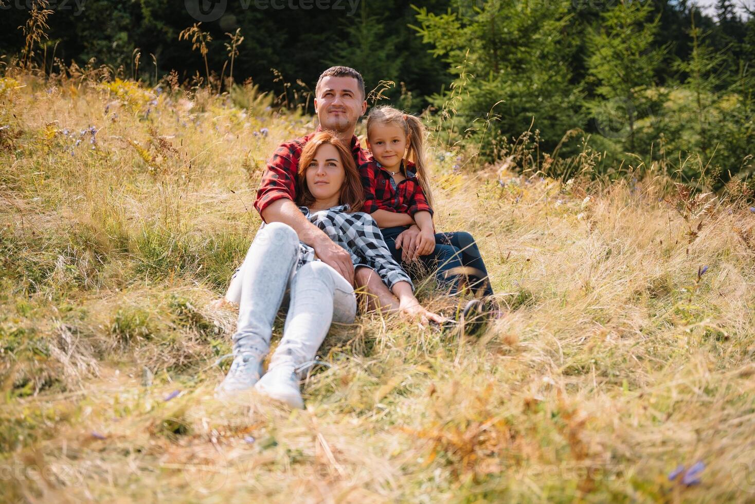 Family of three people rest in the mountains. They sat down to rest, drink water after a hard climb to the mountain. They are tired but happy. photo