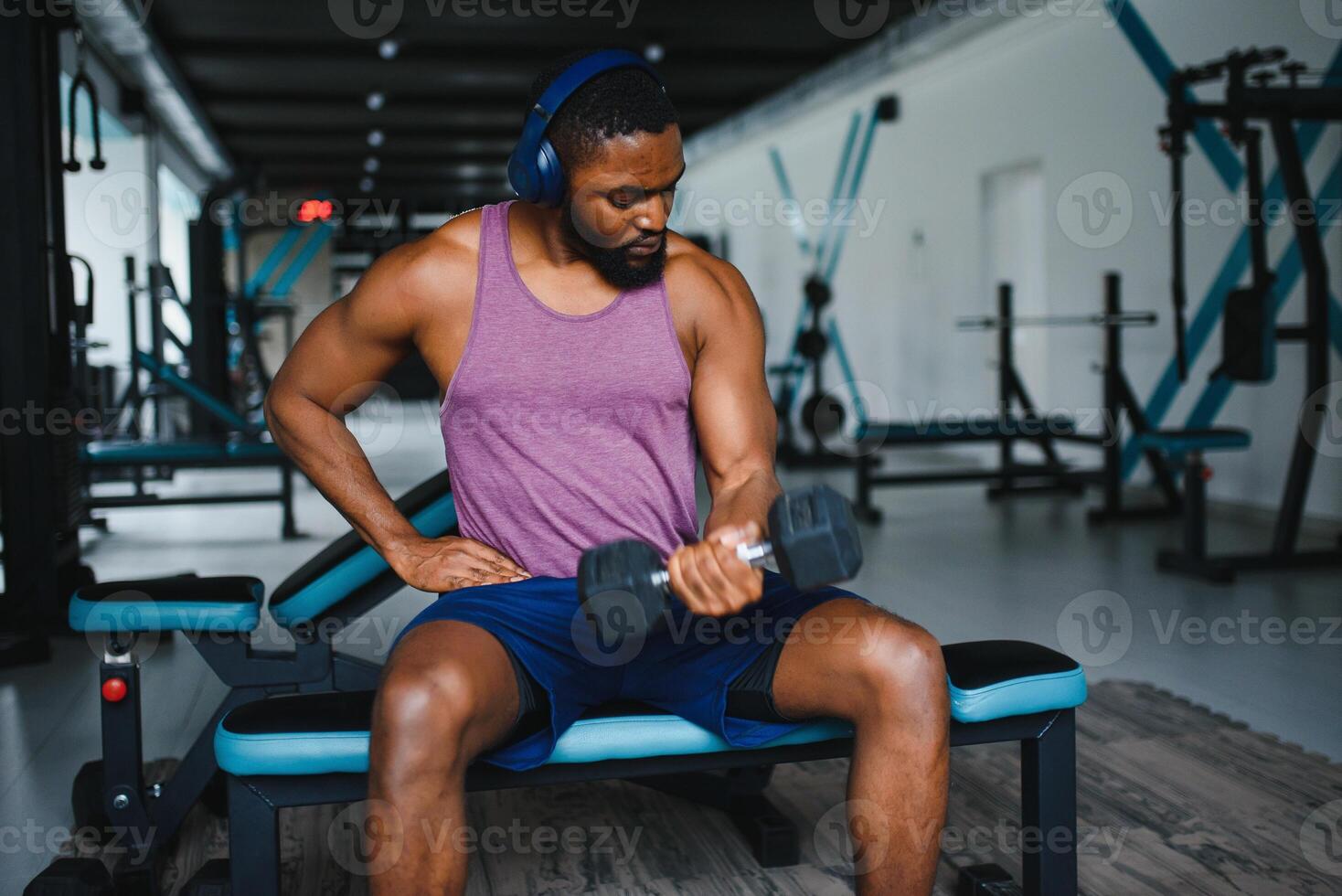 joven africano americano hombre sentado y levantamiento un pesa cerca a el estante a gimnasia. masculino peso formación persona haciendo un bíceps rizo en aptitud centro. foto