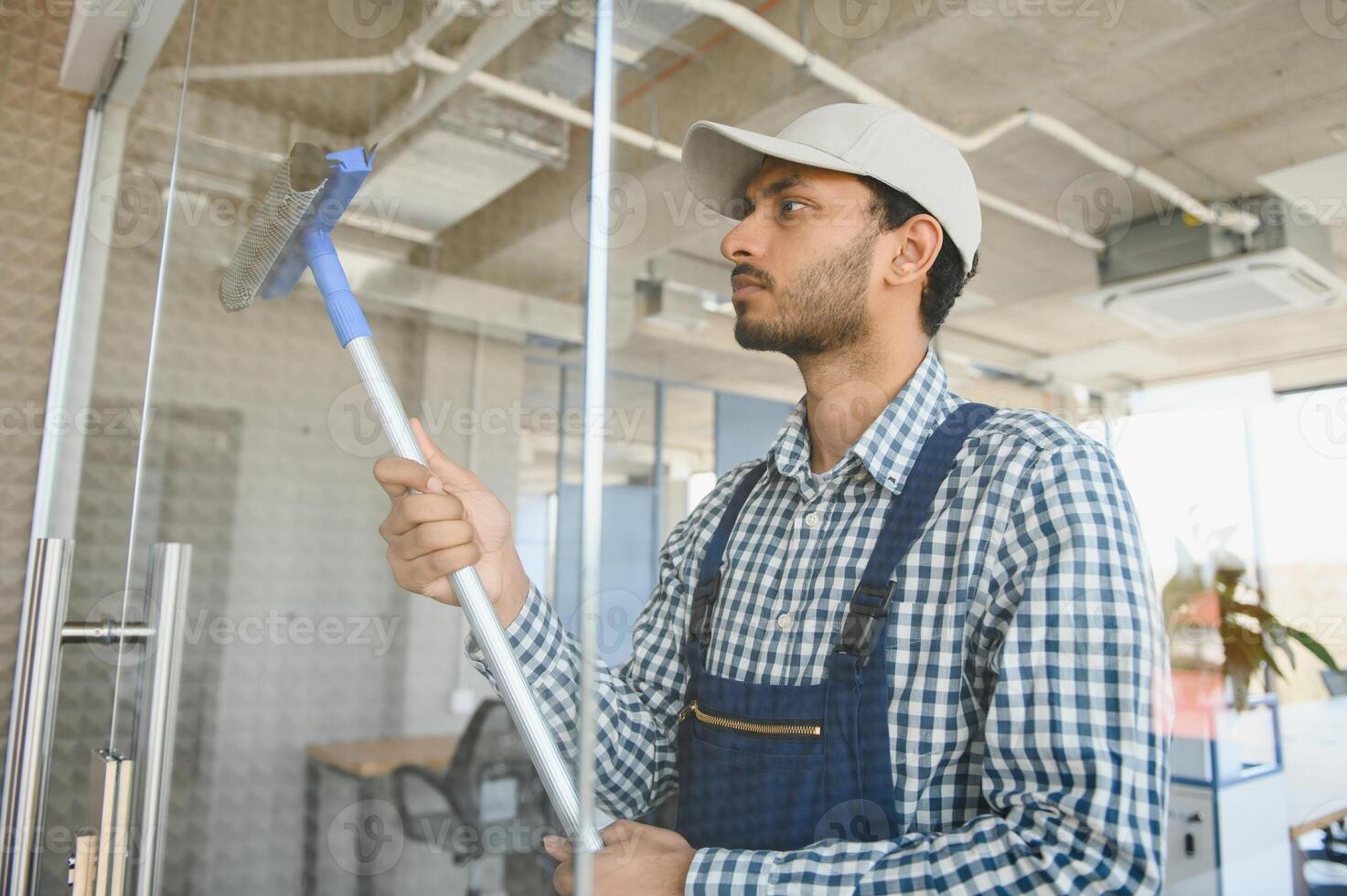 Indian Male professional cleaning service worker cleans the windows and shop windows of a store with special equipment photo