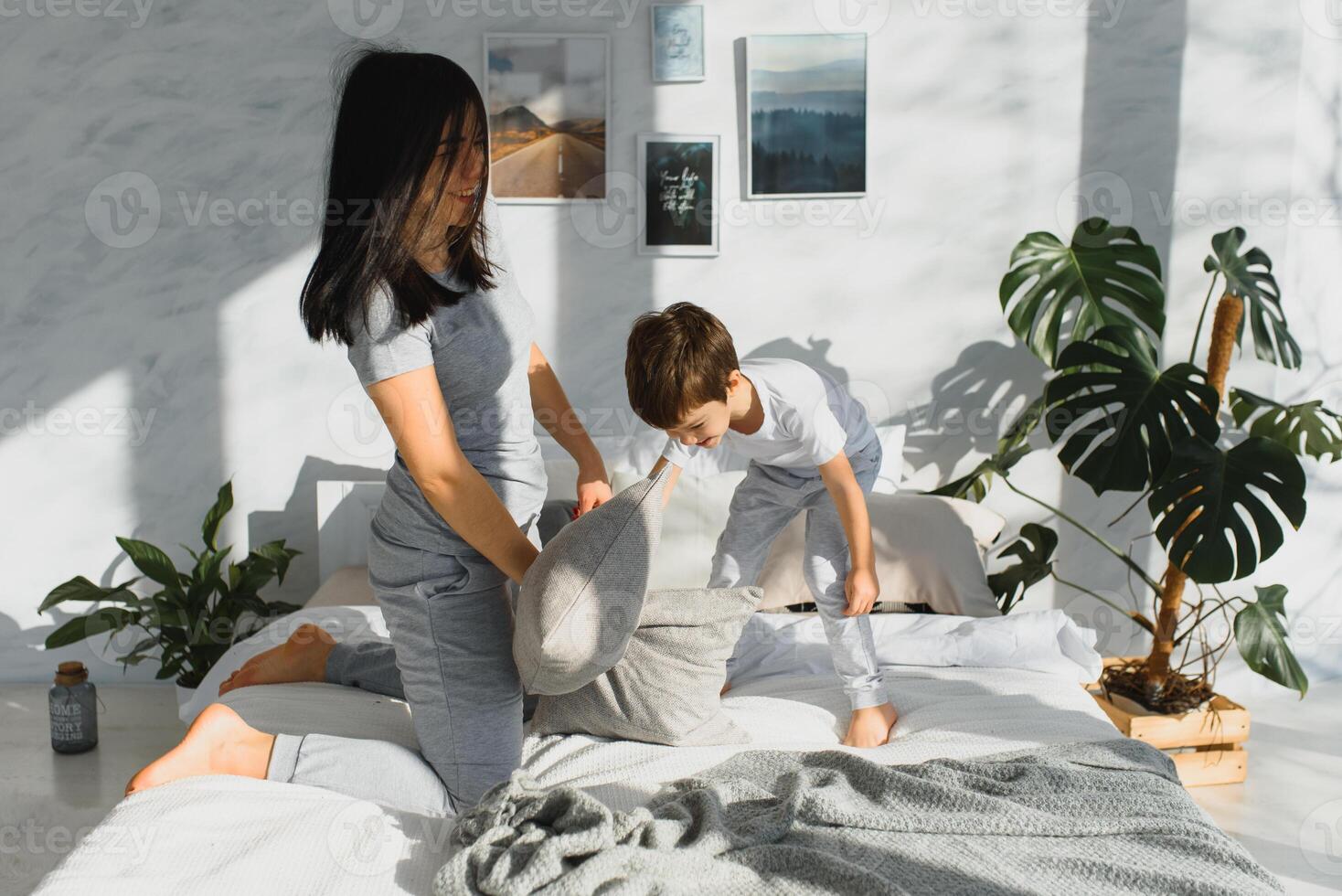happy mother and son fighting with pillows in bed on weekend morning photo