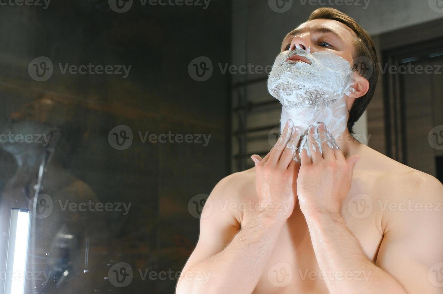 Shaving cream. Morning hygiene procedures. Grooming treatment. Handsome cheerful shirtless man showing applying foam on skin photo