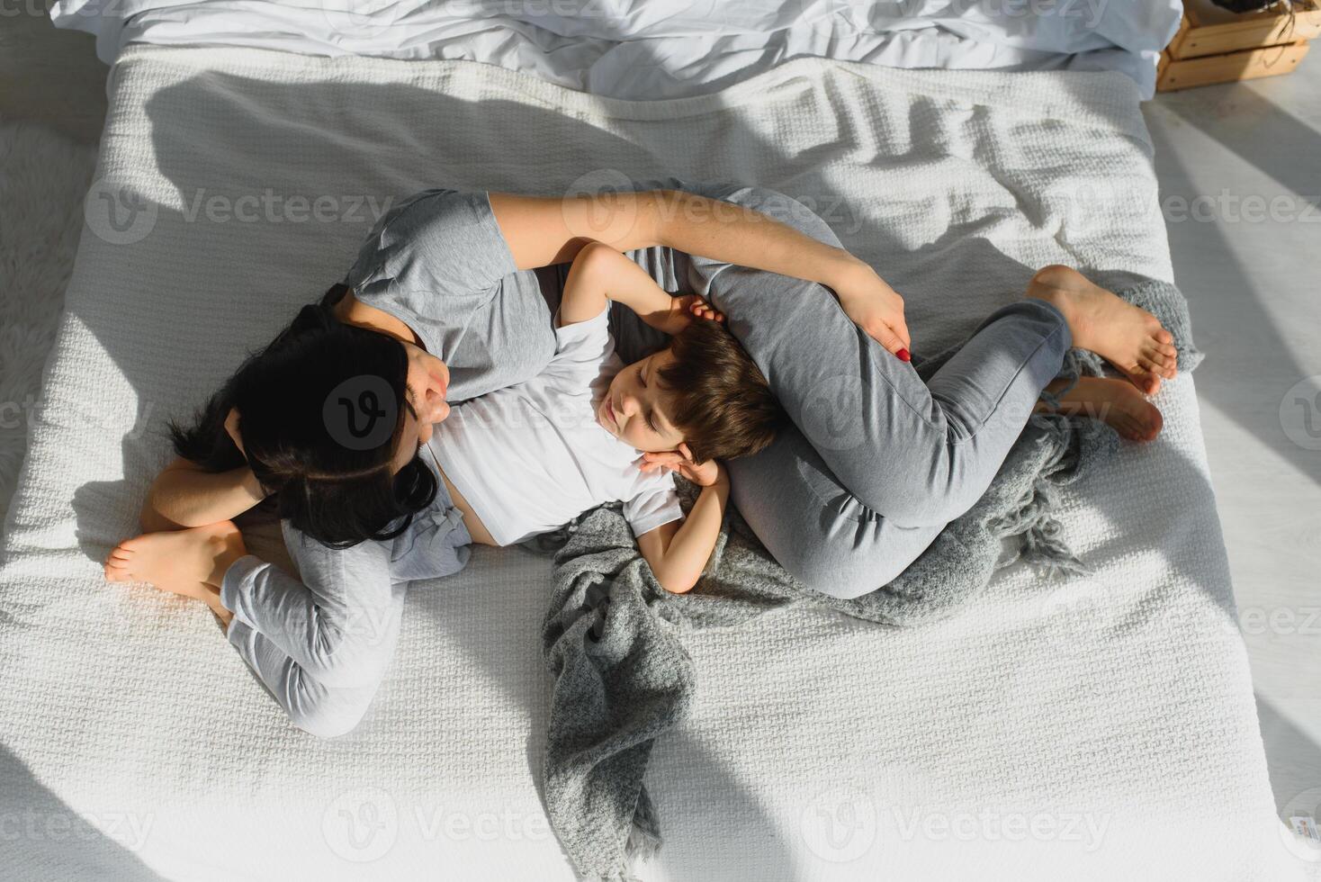 joven madre con su 4 4 años antiguo pequeño hijo vestido en pijama son relajante y jugando en el cama a el fin de semana juntos, perezoso mañana, calentar y acogedor escena. foto