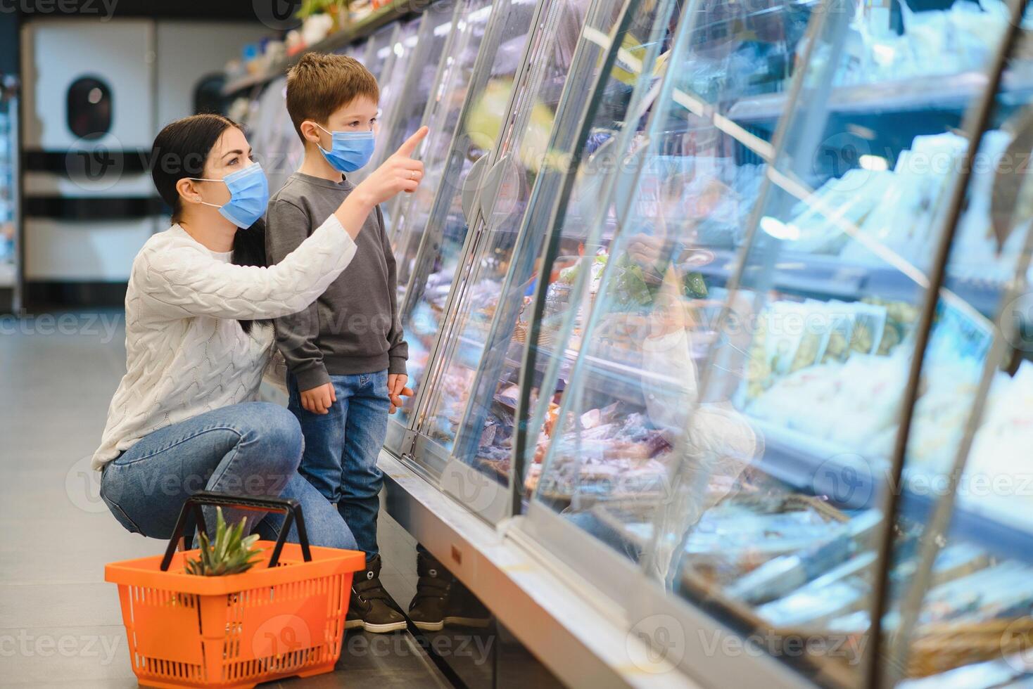 compras con niño durante virus brote. madre y niño vistiendo quirúrgico cara máscara comprando Fruta en supermercado. mamá y pequeño chico comprar Fresco vegetal en tienda de comestibles almacenar. familia en tienda foto