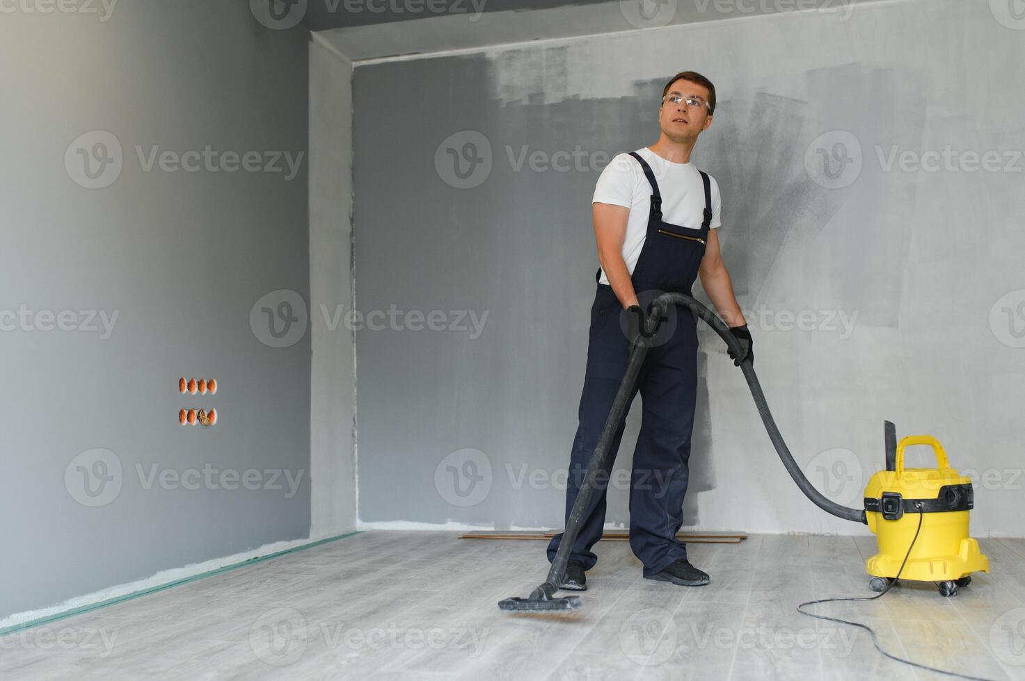 male worker in overall vacuum cleaning during apartment renovation photo