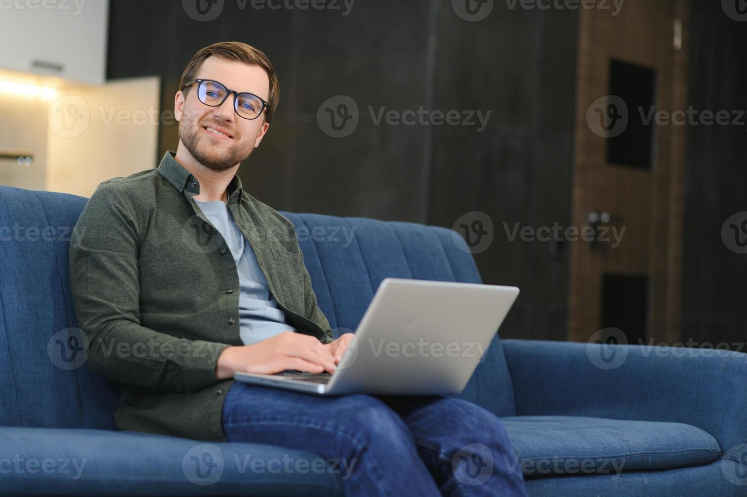 hombres trabajando en ordenador portátil computadora en su habitación. hogar trabajo o estudiar, Lanza libre concepto. joven hombre sentado relajado en sofá con ordenador portátil. moderno empresario utilizando ordenador portátil. foto