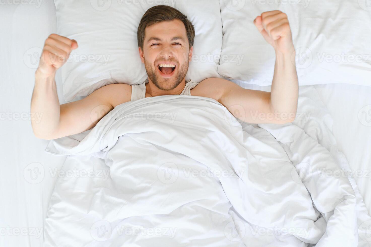 Cheerful Man Waking Up Lying In Cozy Bed At Home On Weekend Morning. Healthy Sleep Concept photo