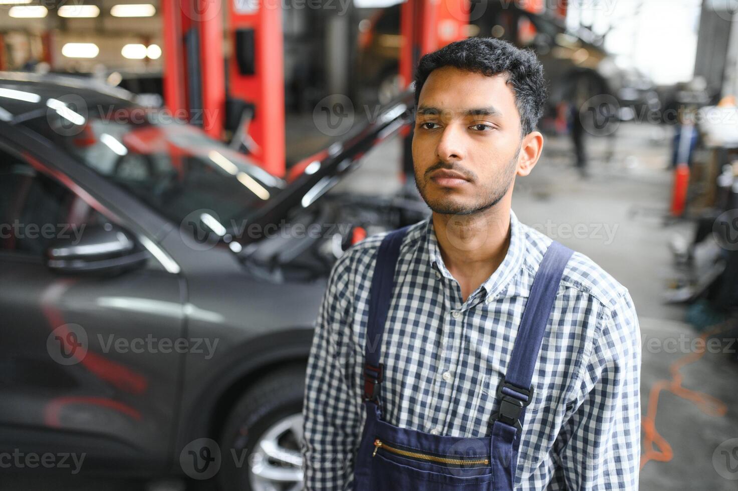 latín Hispano auto mecánico en uniforme es examinando un coche mientras trabajando en auto Servicio foto