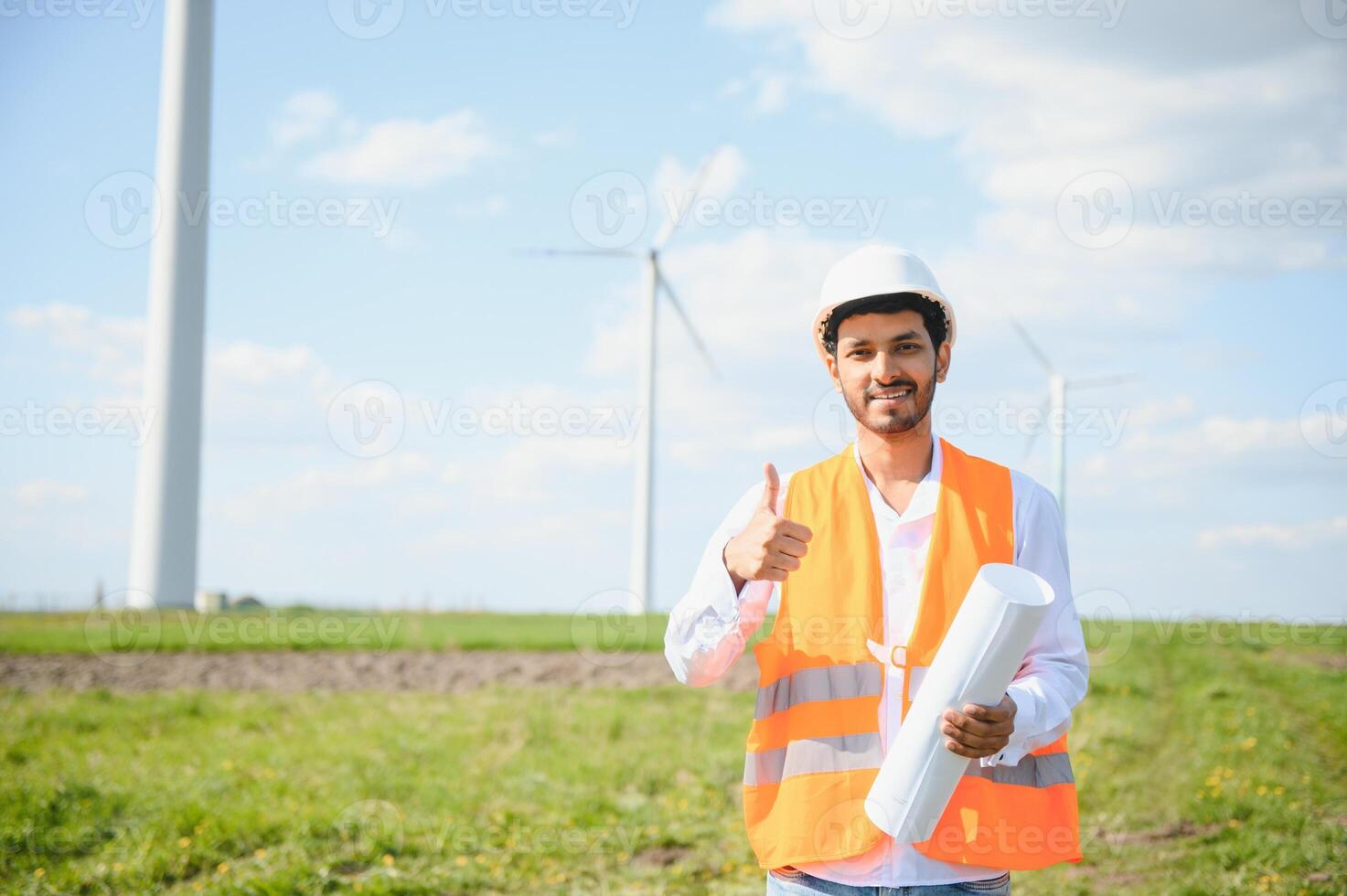 Portrait of focused indian man standing on field with wind turbines photo