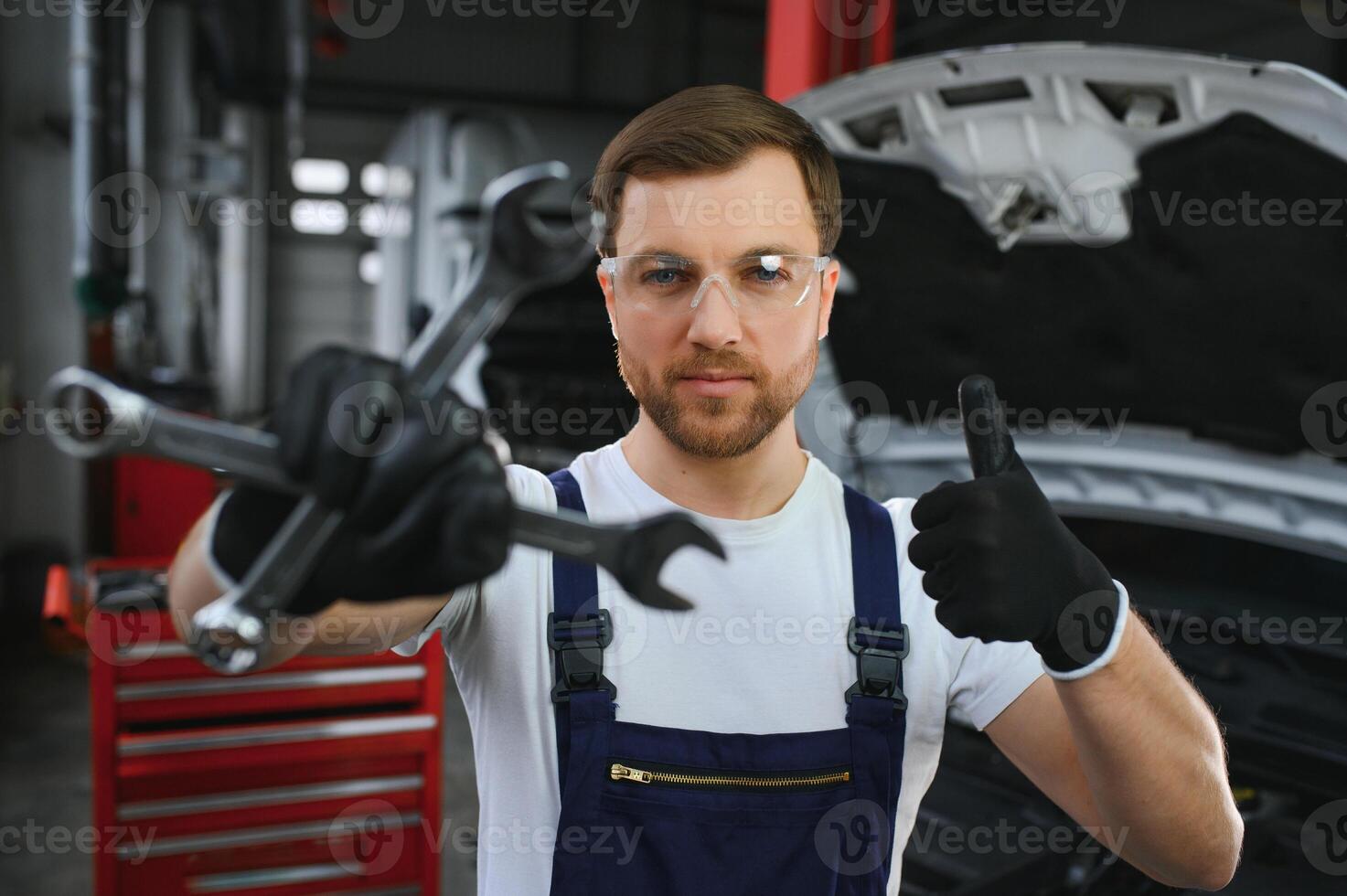 With tool in hand. Adult man in colored uniform works in the automobile salon photo