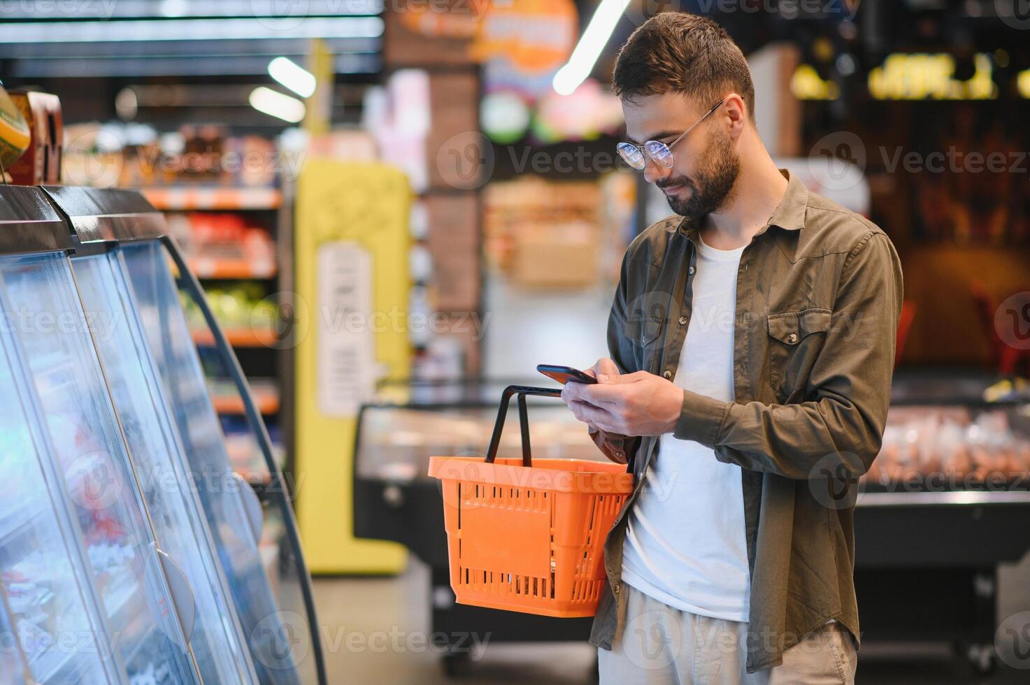 Quick text during shopping. Handsome young man holding mobile phone and smiling while standing in a food store photo