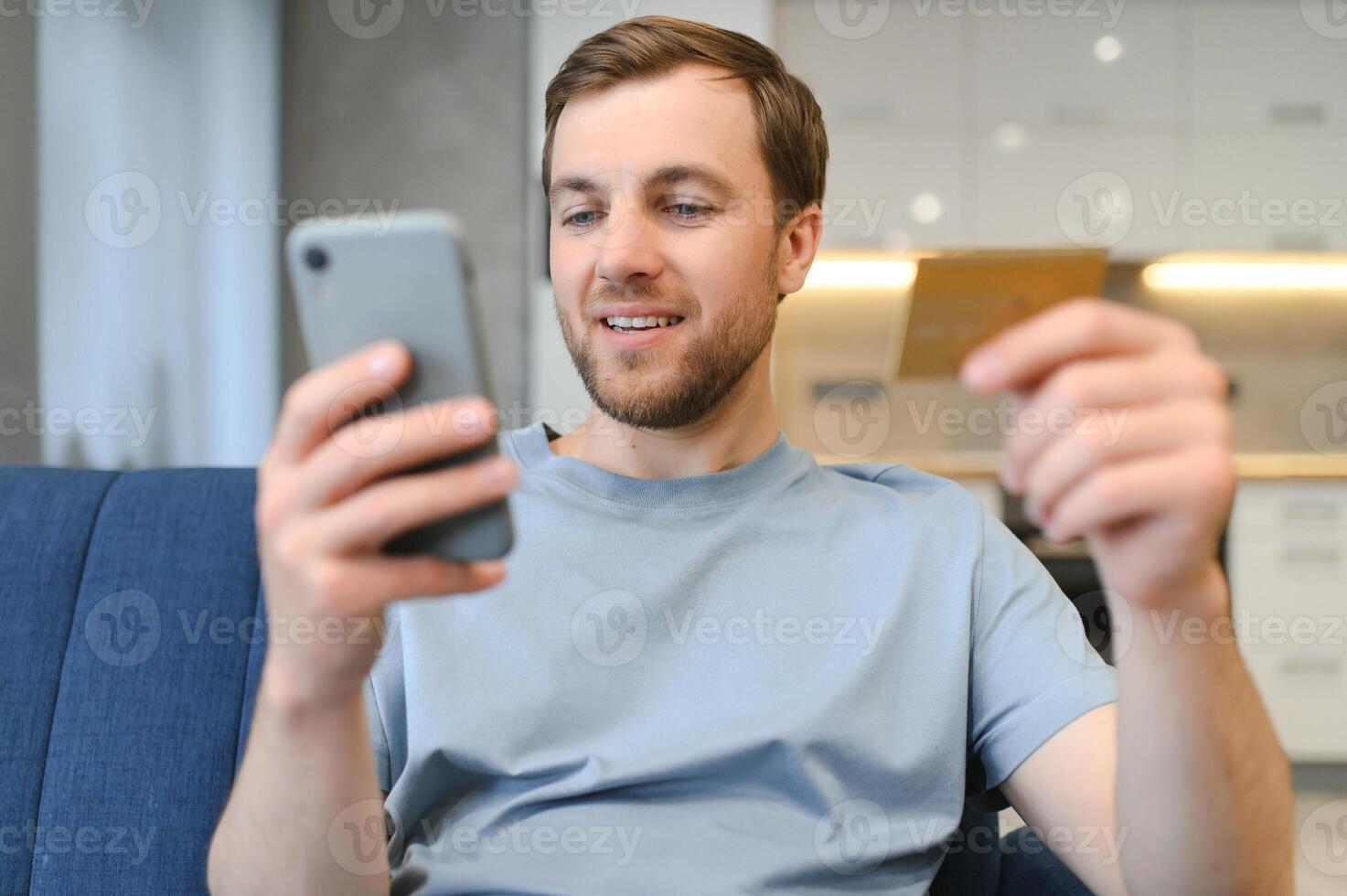 Happy Caucasian man buying things online, using smartphone, laptop and credit card, enjoying shopping in internet. Positive young guy purchasing goods on web, making remote payment photo