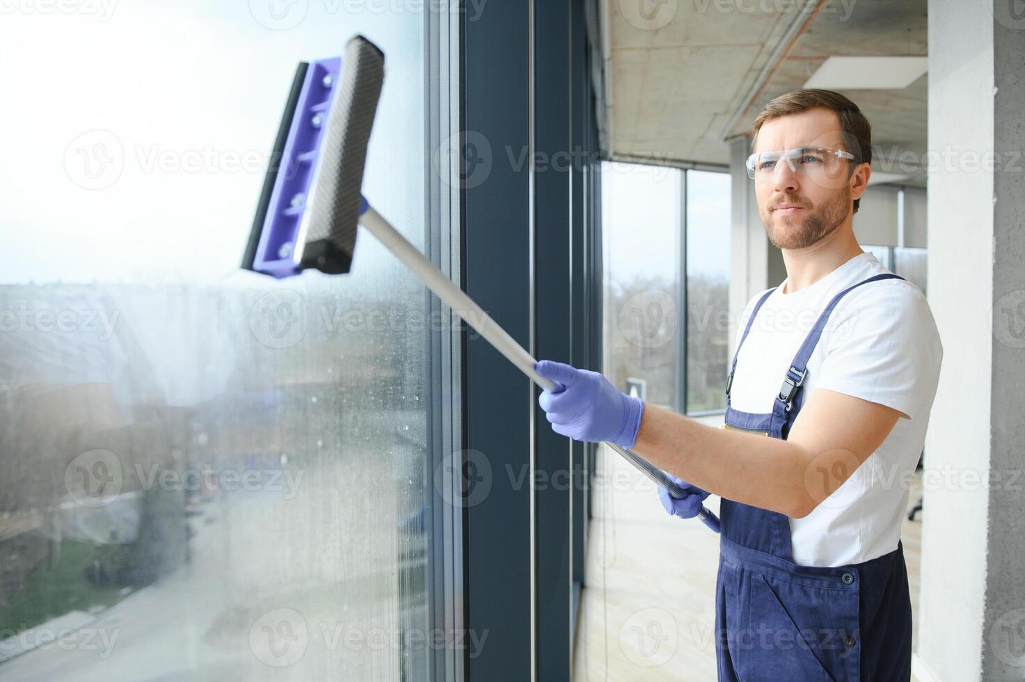 Male professional cleaning service worker in overalls cleans the windows and shop windows of a store with special equipment. photo